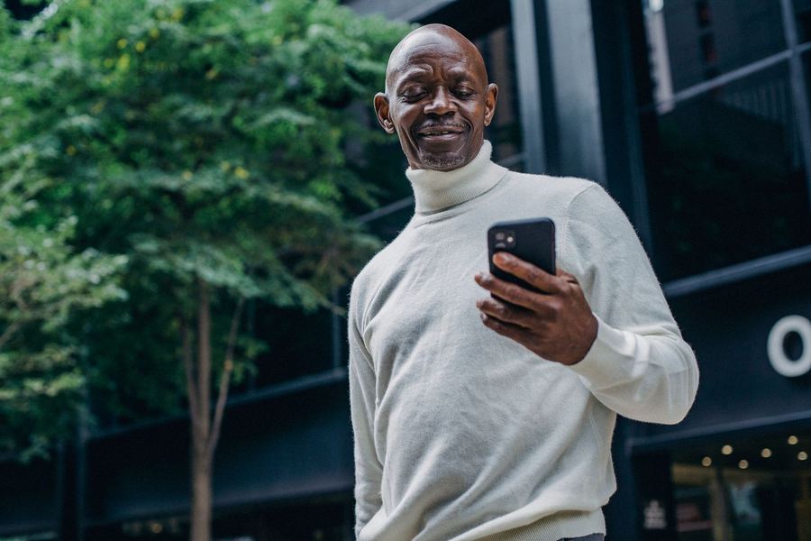 A man smiling at his phone on a city street